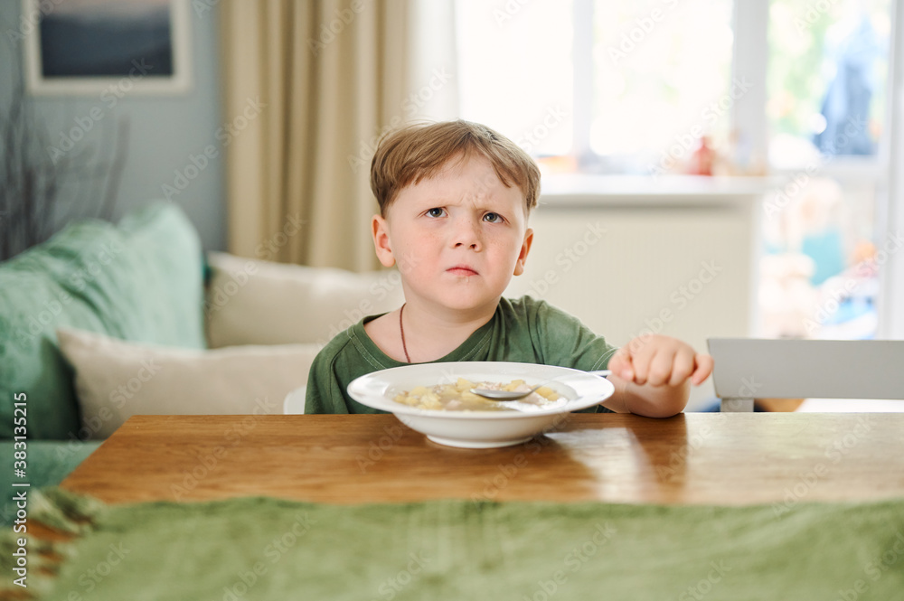 Little preschool child eating soup on the kitchen and sitting on the table Little preschool child eating soup on the kitchen and sitting on the table