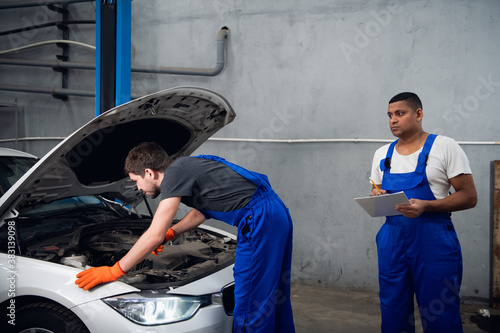 The worker repairs the engine of the vehicle. His colleague writes the results