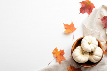 Wooden bowl with pumpkins, dry maple leaves and beige fabric on white background. Flat lay, top view. Autumn fall, harvest, thanksgiving concept.
