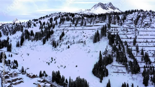 Mountain peak and snow landscape in the alps. Rocks and trees on the walls. Rural areal view in cloudy cold winter