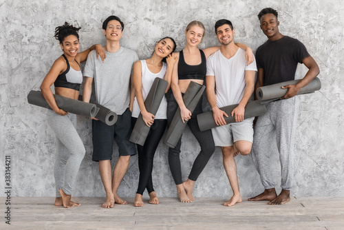 Fitness Class. Sporty multiethnic people with yoga mats posing near gray wall