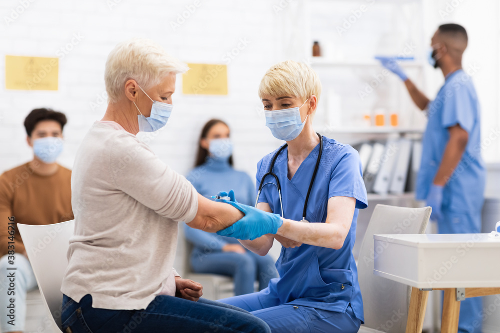 Fototapeta premium Senior Woman Receiving Coronavirus Vaccine Injection Sitting With Doctor Indoor