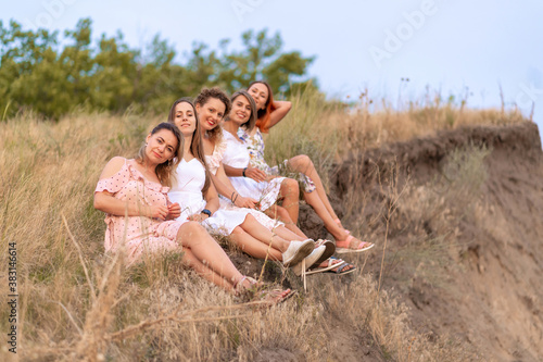A cheerful company of beautiful girls friends enjoy a picturesque panorama of the green hills at sunset