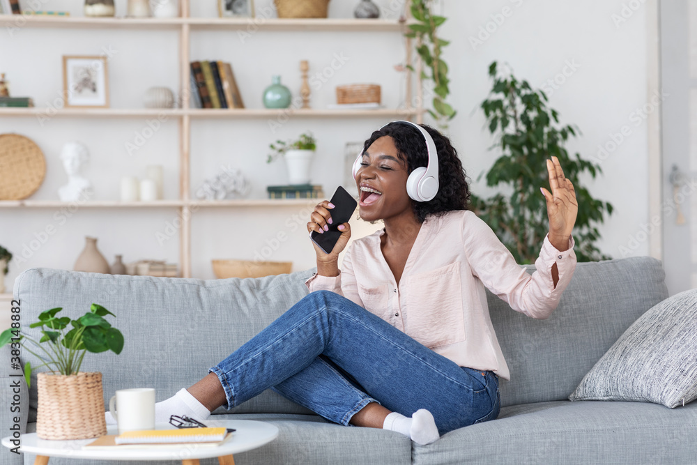 Fototapeta premium African Lady Listening Music And Singing At Home, Using Smartphone As Microphone