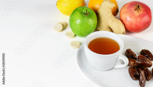 Fruit tea cup, dates on the white saucer. Tropical citrus fruits, ginger and multivitamins pills on the white background. Autumn, seasonal relaxing concept.