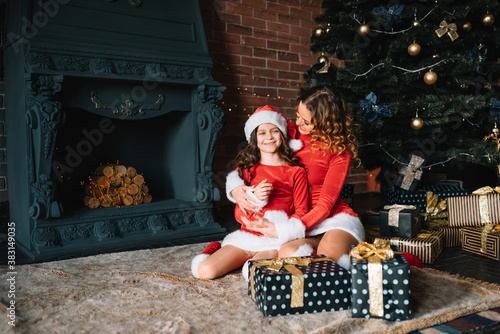Merry Christmas and Happy Holidays! Cheerful mom and her cute daughter girl in Christmas costumes exchanging gifts.