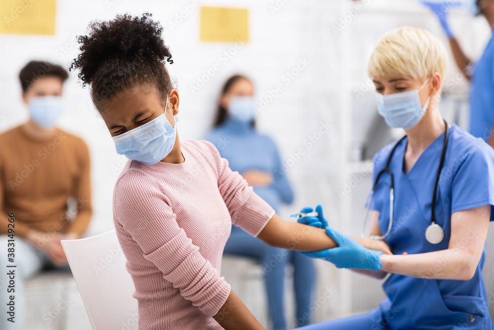 Obraz premium Black Teen Girl Receiving Covid-19 Vaccine Injection In Hospital Room