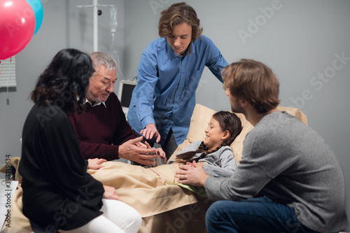 A family visiting a pretty, little girl, who is lying in bed at a hospital ward.