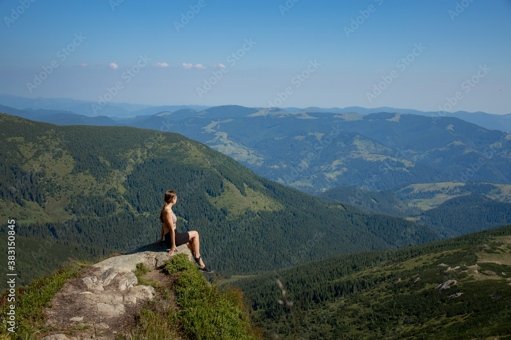 A girl sits on the edge of the cliff and looking at the sun valley and mountains