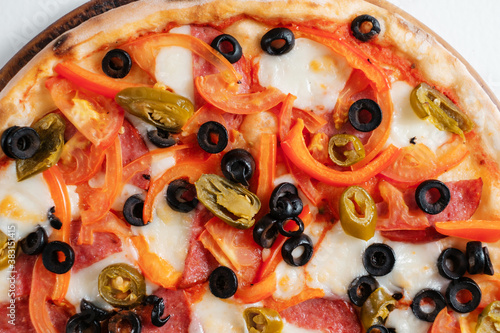 Italian pizza with ham, olives, peppers and herbs close-up.