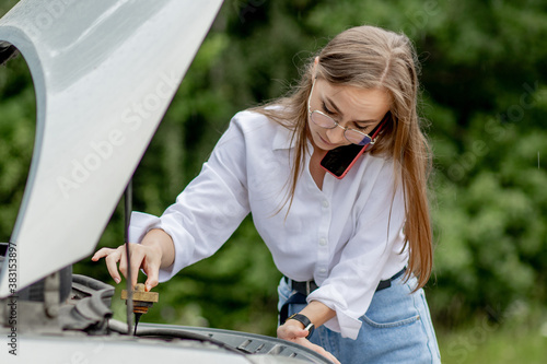 Young woman standing near broken down car with popped up hood having trouble with her vehicle. Waiting for help tow truck or technical support. A woman calls the service center © volody10
