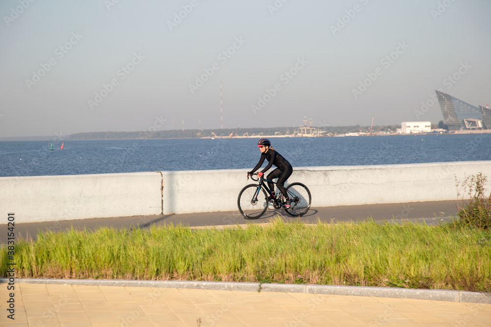 Obraz premium A woman rides a bicycle along the embankment. Riding a bicycle. Outdoor sports. Embankment of the Gulf of Finland Russia St. Petersburg.Cycling workout