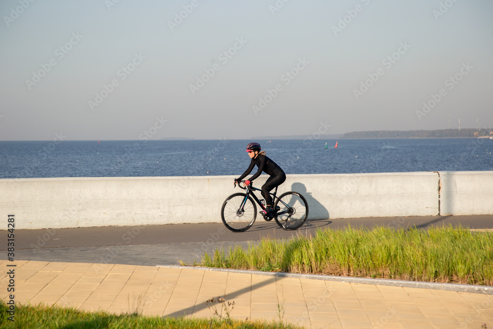 Obraz premium A woman rides a bicycle along the embankment. Riding a bicycle. Outdoor sports. Embankment of the Gulf of Finland Russia St. Petersburg.Cycling workout