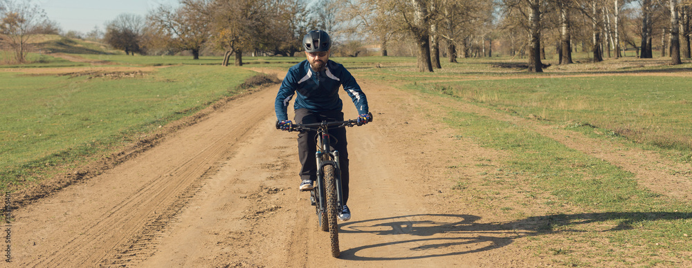 Fototapeta premium Cyclist in pants and fleece jacket on a modern carbon hardtail bike with an air suspension fork rides off-road. The guy is resting on a bench in the autumn park.