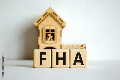 Wooden cubes form the word 'FHA, federal housing administration' near miniature house. Beautiful white background, copy space. business concept.