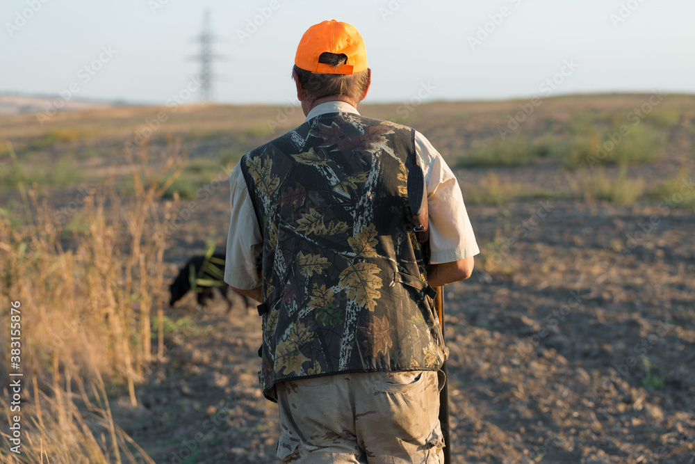 Duck hunter with shotgun walking through a meadow. .Rear view of a man with a weapon in his hands. Duck hunter with shotgun walking through a meadow. .Rear view of a man with a weapon in his hands.