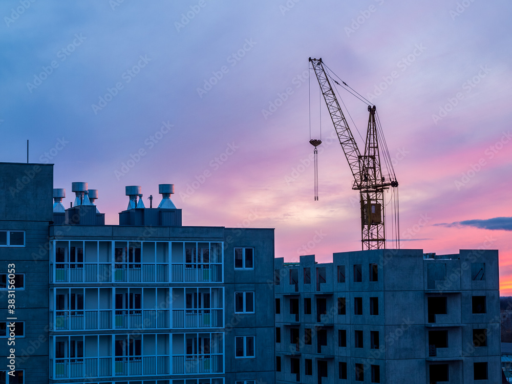 high-rise crane in the construction of high-rise buildings in the city district, against the background of the sunset
