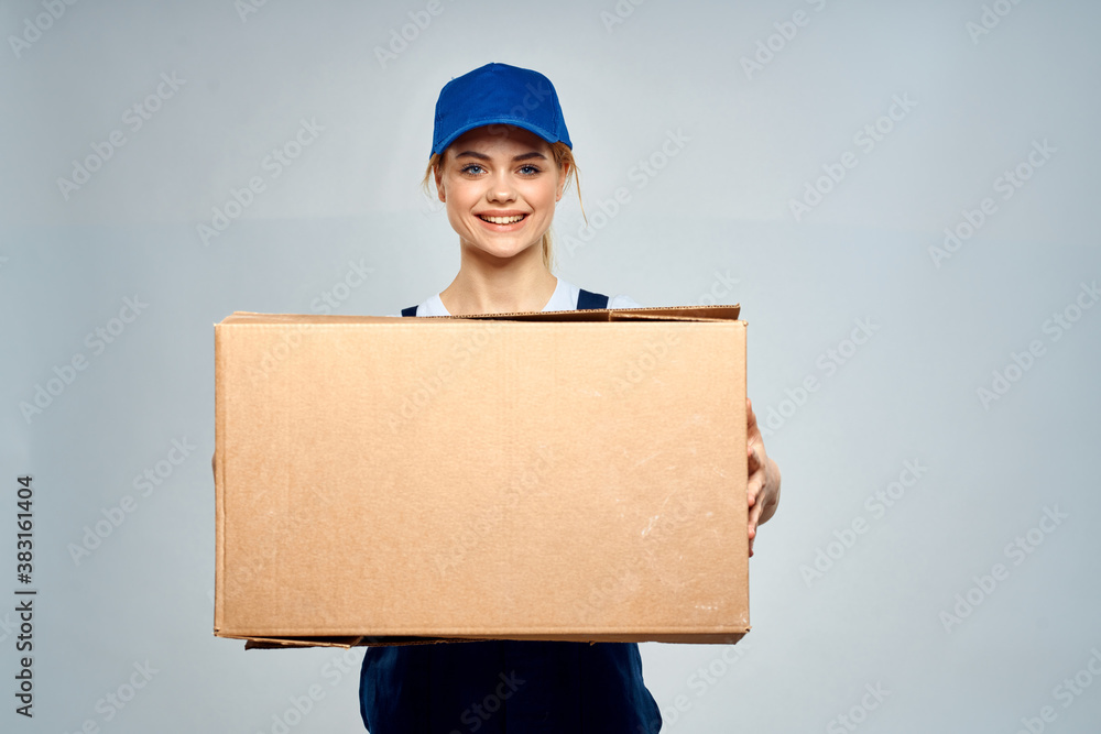 A woman in a working uniform with a box in the hands of a delivery service delivery service light background A woman in a working uniform with a box in the hands of a delivery service delivery service light background