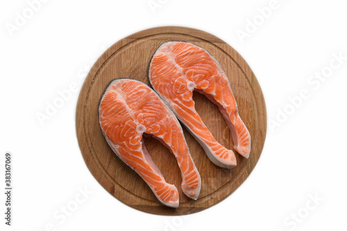 There are two steaks of red fish on a round wooden cutting board. On white clipping background
