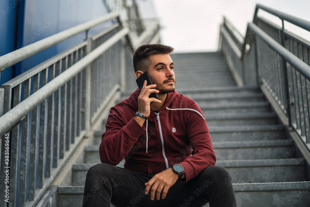 Chico joven sentado en escalera metalica junto a edificio azul Chico joven sentado en escalera metalica junto a edificio azul