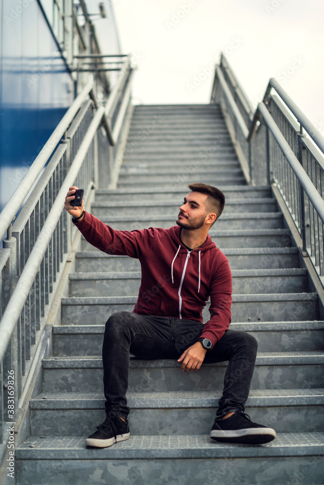 Chico joven sentado en escalera metalica con teléfono movil Chico joven sentado en escalera metalica con teléfono movil