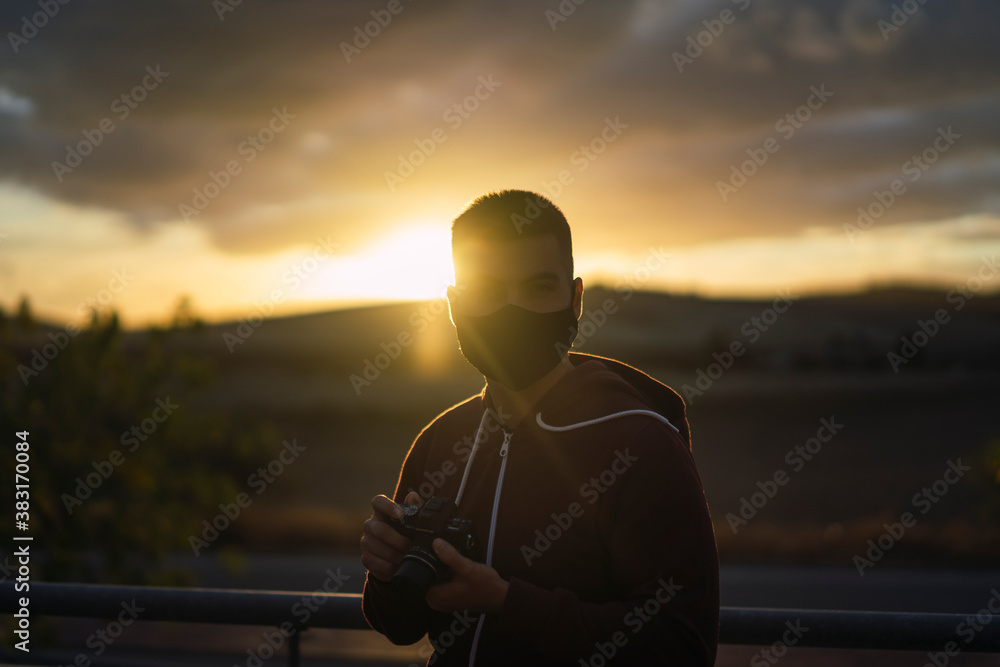 Fototapeta premium Chico joven con mascarilla negra con el atardecer de fondo