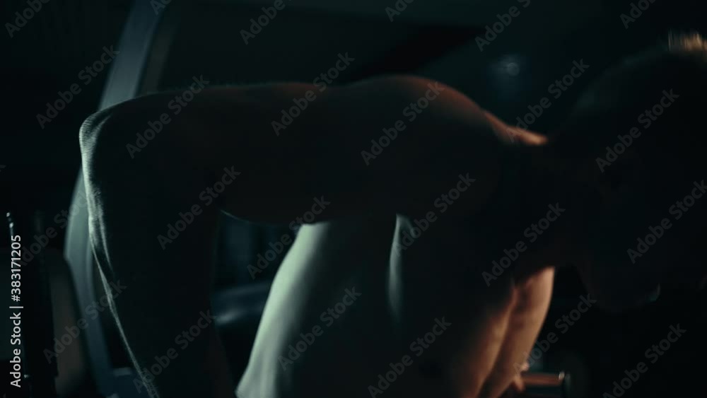 A muscular man performs exercises squeezes out on uneven bars in a dark gym, lifting weights A muscular man performs exercises squeezes out on uneven bars in a dark gym, lifting weights