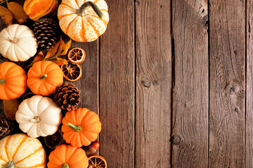 Autumn side border of pumpkins and natural fall decor. Overhead view on a rustic dark wood background with copy space.