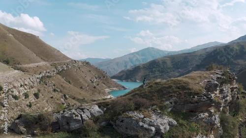 Woman girl runs up rocky hill near picturesque Bylym gizhgit lake with azure water in valley among mountains on sunny day panoramic aerial view photo