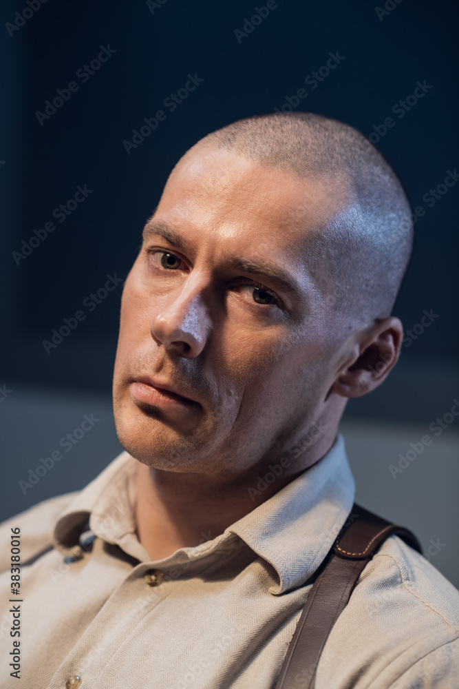 Bald investigator tired after questioning, portrait. A brutal man with a gun holster in a dark room with dramatic light Bald investigator tired after questioning, portrait. A brutal man with a gun holster in a dark room with dramatic light