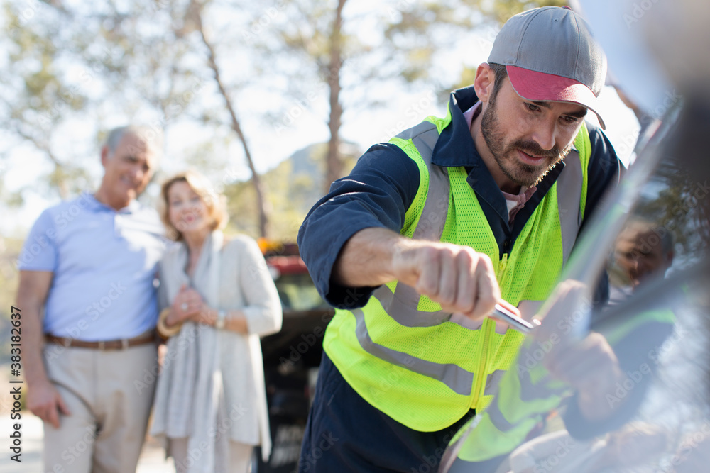 Naklejka premium Senior couple watching male roadside assistance mechanic fix car