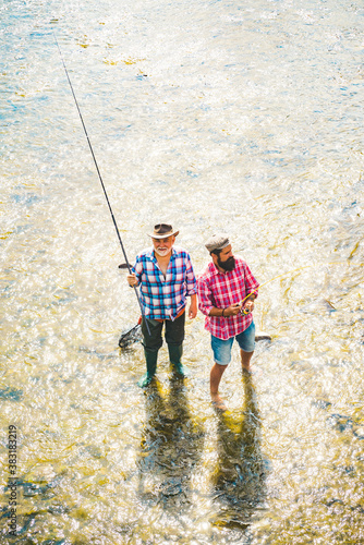 Father and adult son fishing lakeside. Man bearded fisher. Mature man fly fishing. Keep calm and fish on. Luxury life concept. Senior man gone fishing.