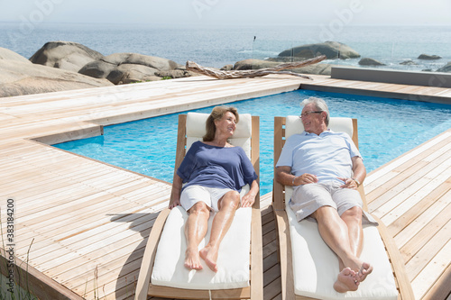 Photography Senior couple relaxing on lounge chairs at sunny ocean poolside
