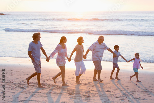 Multi-generation family holding hands and walking on sunny beach