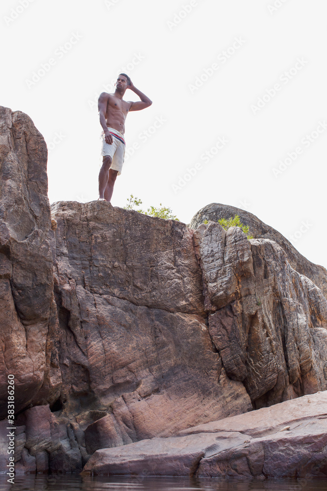 Fototapeta premium Young man in swim trunks on rocks