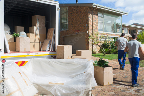 Movers carrying boxes from moving van in sunny driveway