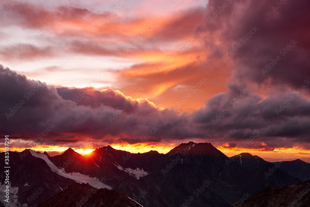 Sunset in mountains. Reflection of red sun on mountain snow peaks and clouds. Altai, Belukha area