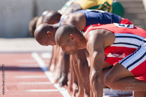 Foto Focused male track and field athletes at sunny starting line