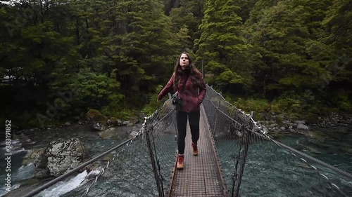 Woman walking across rope bridge over river in the forest