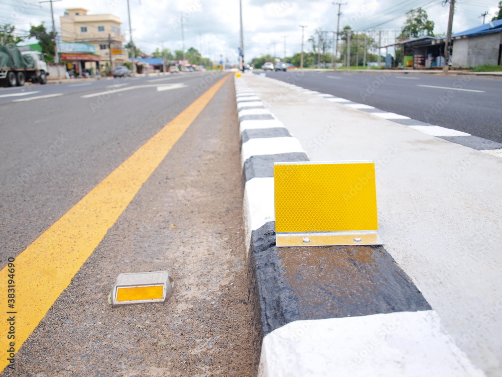 Reflector on median strip. Yellow road markings and concrete curb dividers  to increase the safety of traffic on the road. On the background of  buildings and blue sky. Selective focus foto de