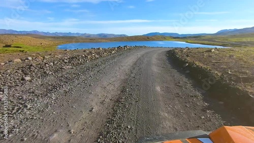 An adventurous trip in buggy car running at high speed on dirt road parallel to beautiful lake, with camera mounted on the bonnet.