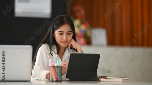 Attractive young woman graphic designer working at home office and using computer tablet on white desk.