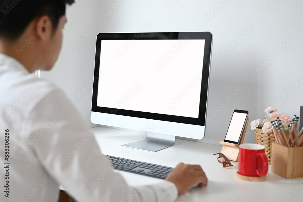 Cropped shot of young man planing his project on computer pc with white screen on white desk. Cropped shot of young man planing his project on computer pc with white screen on white desk.