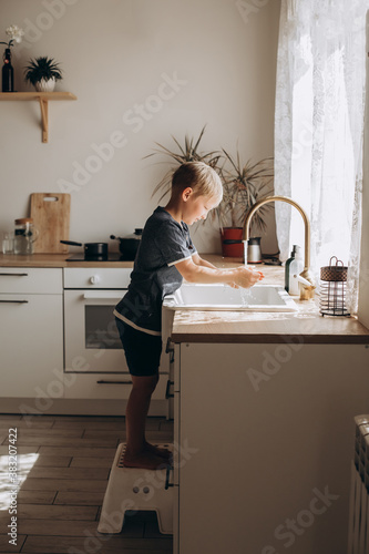 A boy of European appearance washes his hands in a light kitchen at home. 