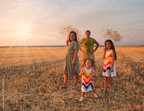 A family of 4 people, stand in a field at sunset, hold dry flowers in their hands and smile in the sun
