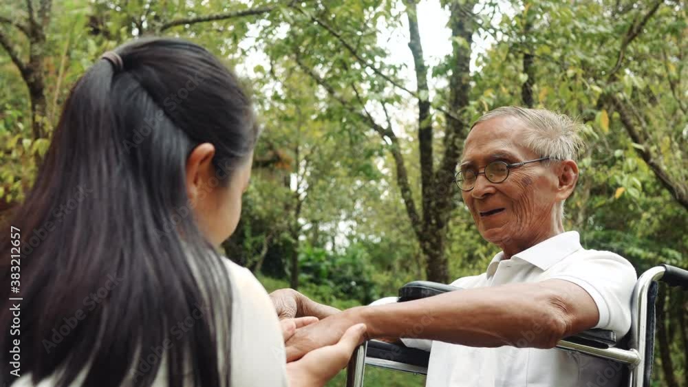 Happy smiling caregiver granddaughter taking care her grandfather sitting on wheelchair while traveling at park. Happy smiling caregiver granddaughter taking care her grandfather sitting on wheelchair while traveling at park.