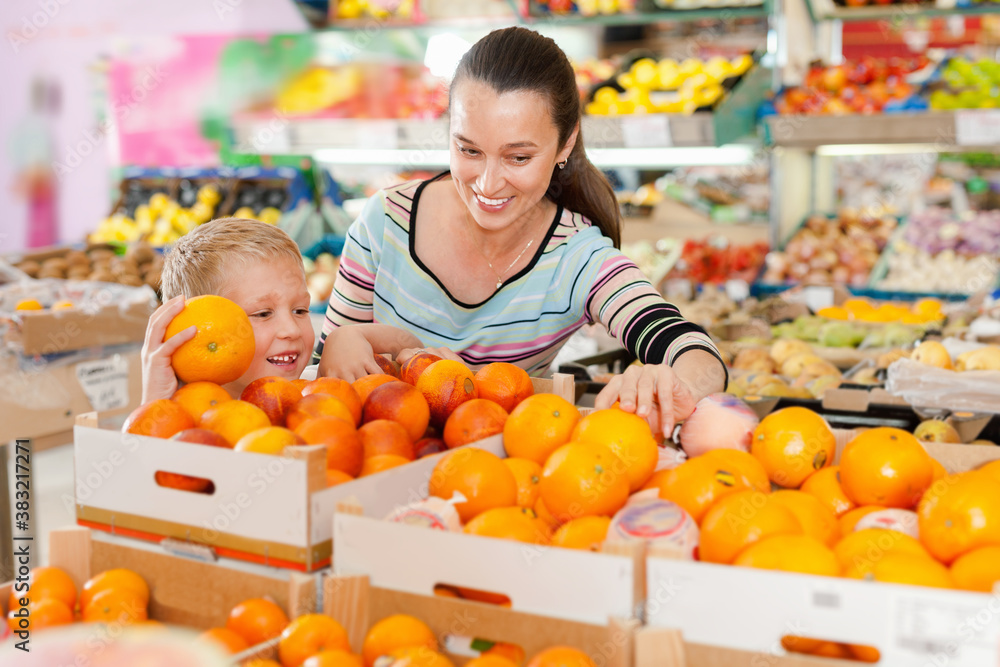 Portrait of positive smiling woman and her little son choosing oranges at shop