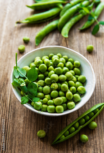 Green peas in white bowl with fresh pods on the wooden table, top view or flat lay