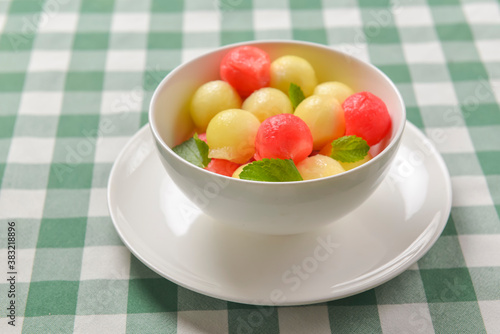 Watermelon granita ice cream. Melon and watermelon sorbet ice cream balls in a white bowl over green plaid table cloth.