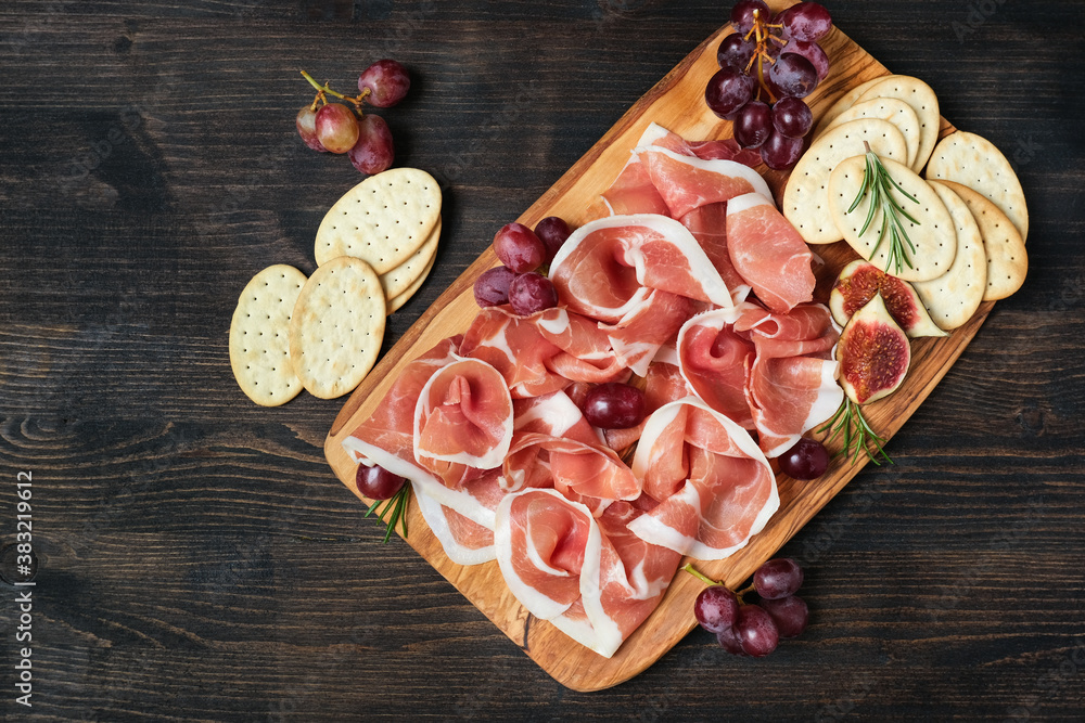 Traditional Italian antipasti prosciutto crudo with grapes and crackers on a wooden plate. Spanish jamon. Food for aperitif and dinner lunch in the restaurant 